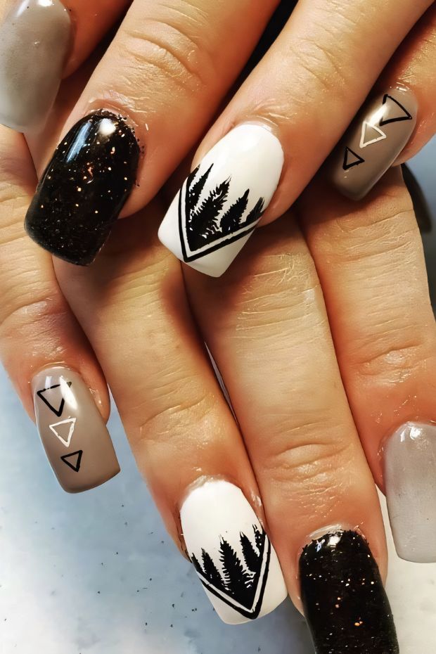 Camping nails with nature-inspired designs, featuring black trees, triangles, and sparkly brown hues.