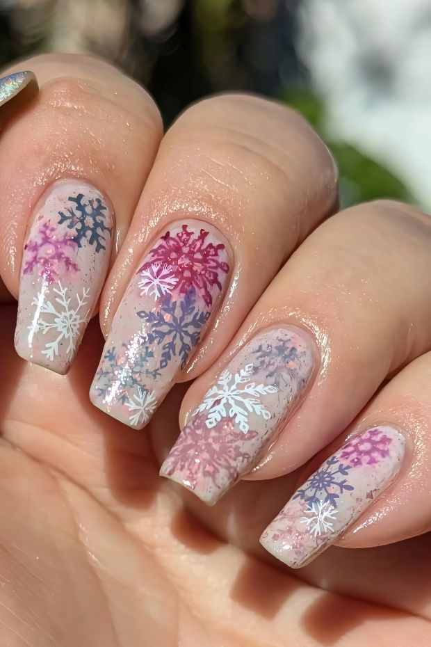 Winter nails with colorful snowflakes in pink and lavender on an elegant ombre background, showcasing a chic seasonal design.