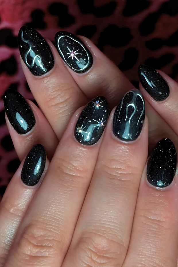 Black nails with cosmic glitter and star accents, featuring elegant line designs and shimmering elements for a galactic look.