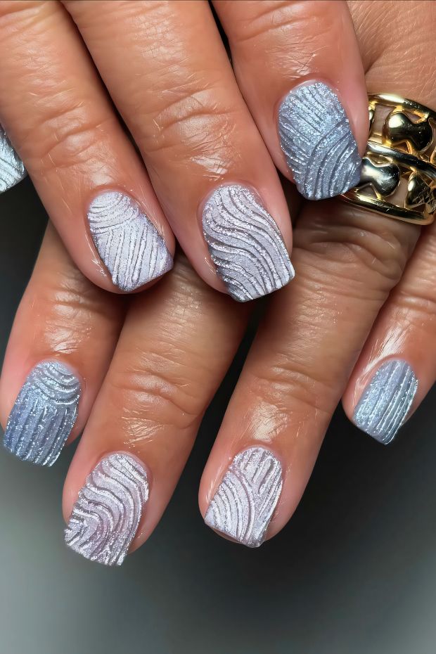 Winter nails featuring icy blue and silver wave patterns with textured finish for a chic, seasonal look.