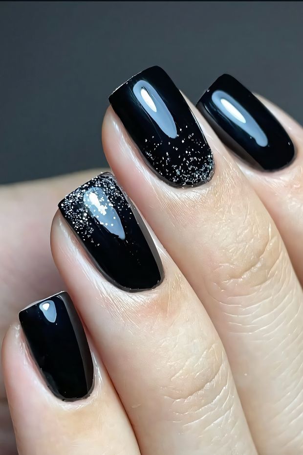 Elegant black nail design with a glossy finish and shimmering glitter accent for a trendy look.