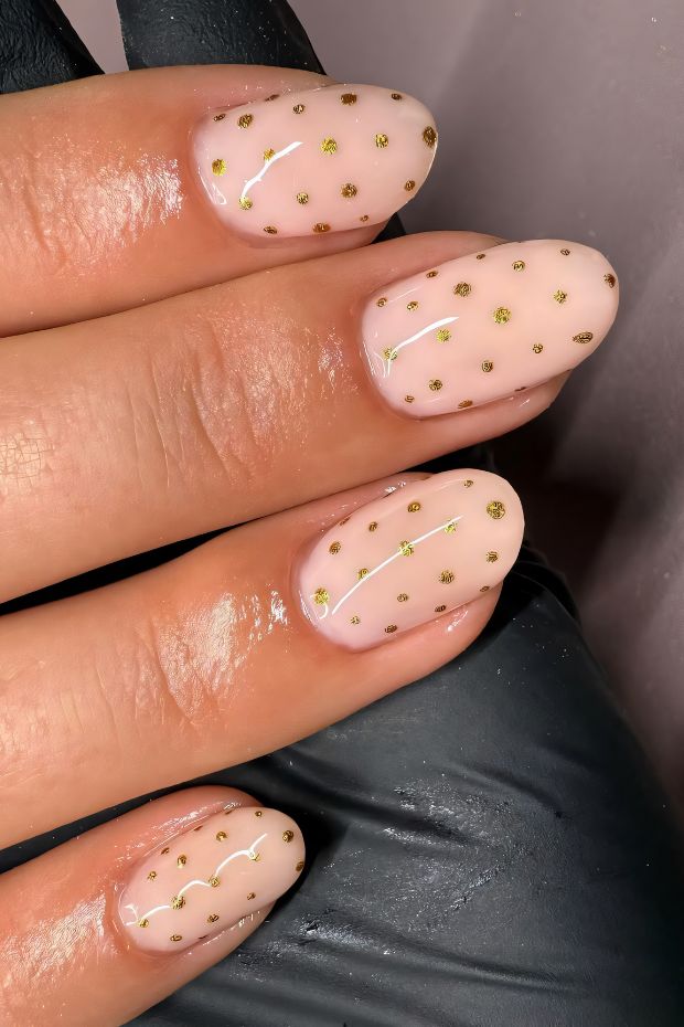 Chic polka dot nail art featuring gold accents on a nude background for a modern and playful look.