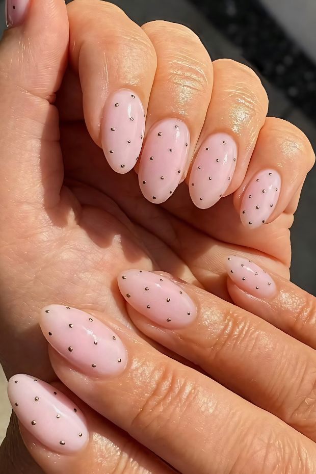 Pink nails with elegant black polka dots for a chic nail art design.