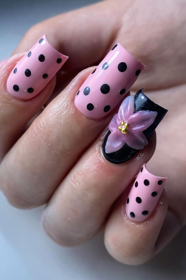 Polka dot nail design with pink and black colors and a floral accent nail.