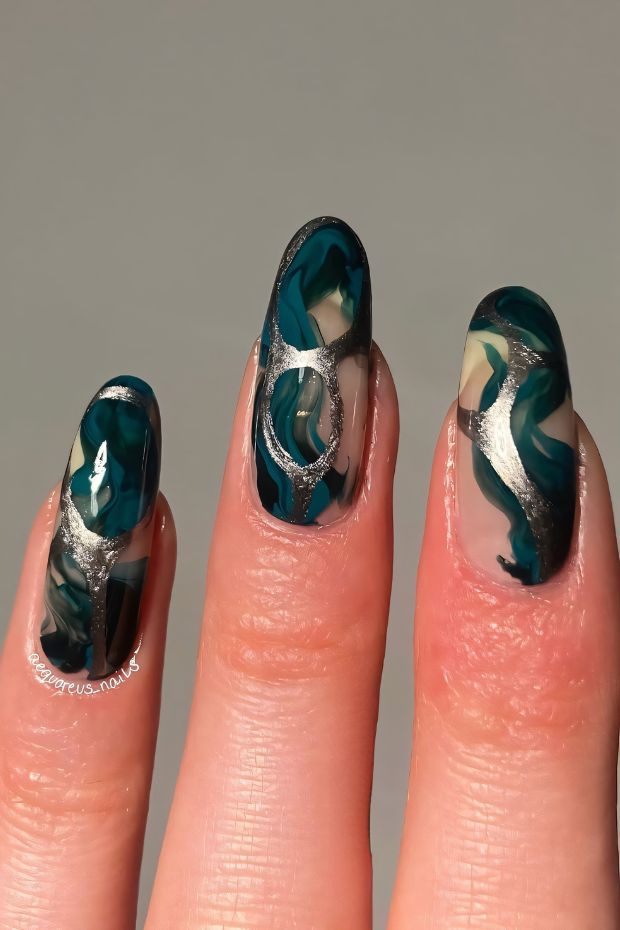 Winter nails featuring abstract green and cream swirls with elegant silver accents for a chic seasonal look.