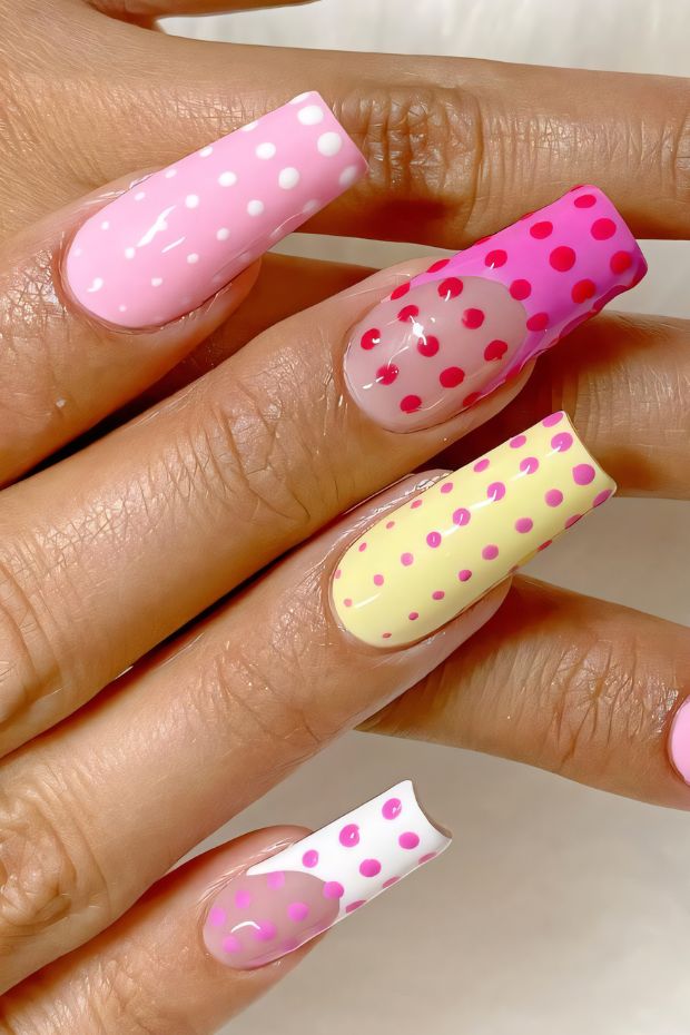 Colorful polka dot nail art design in pink and yellow tones with various dot patterns.