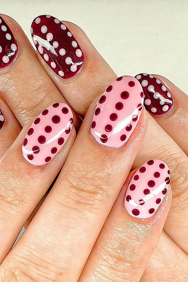 Polka dot nail design featuring pink and burgundy colors with varied dot sizes and silver accents on elegant nails.