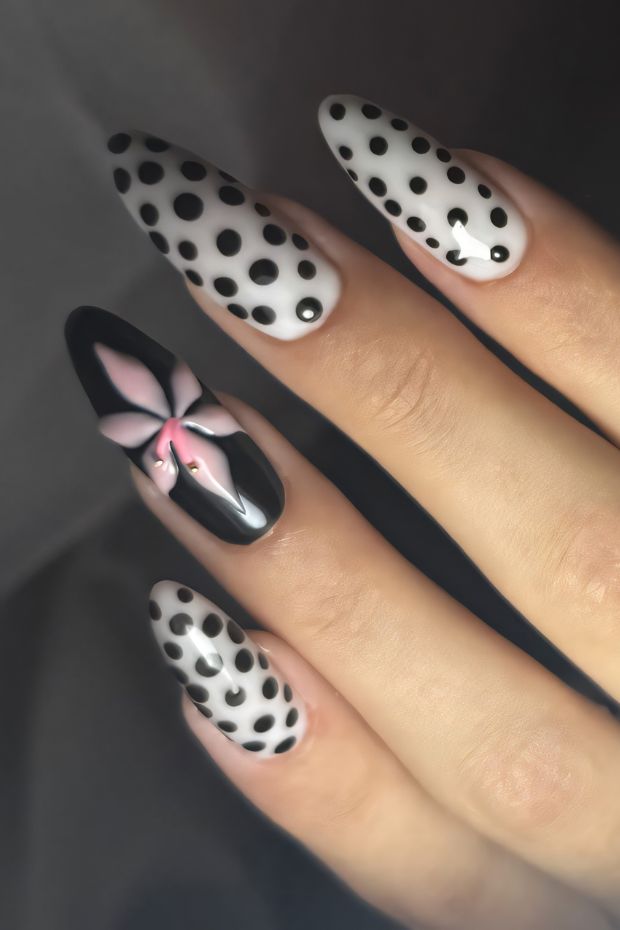 Polka dot nail design with black and white dots and a pink flower accent on a long almond nail.