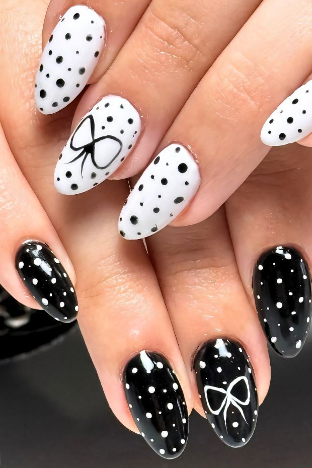 Polka dot nail design featuring black and white patterns with elegant bow accents on long almond-shaped nails.