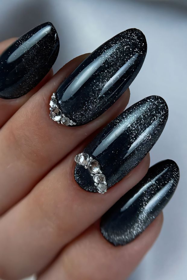 Glamorous black nails with silver glitter accents and intricate rhinestone details for a bold manicure look.