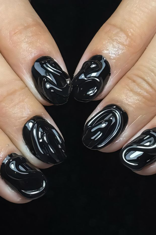Glossy black swirl nail art with intricate patterns for a bold and trendy look.