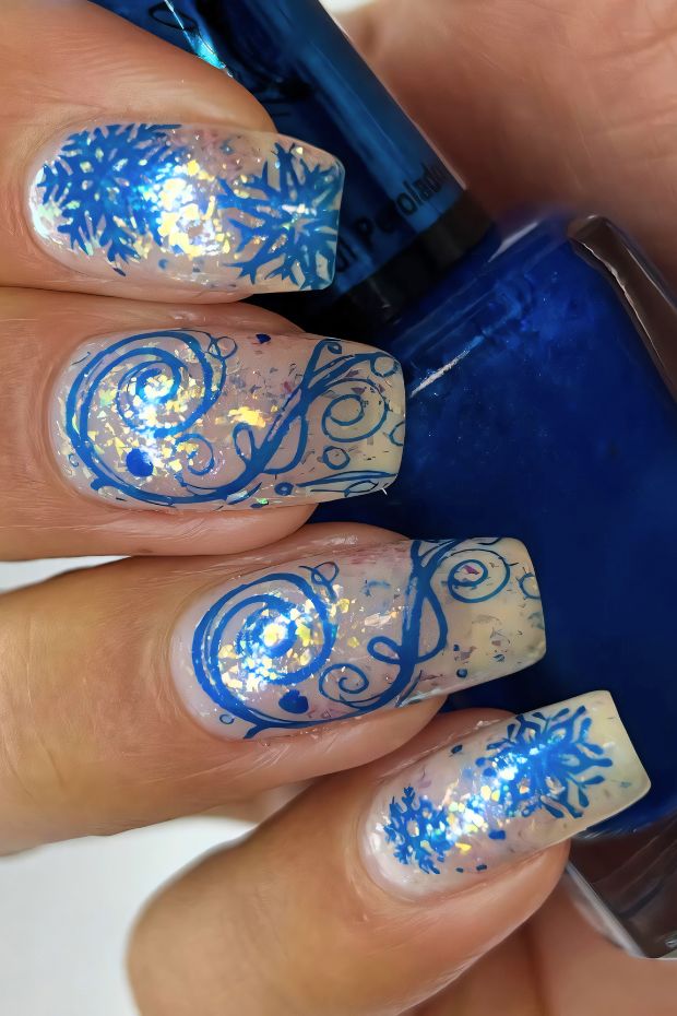 Winter nail art with blue snowflakes, intricate swirls, and glitter for a festive design.