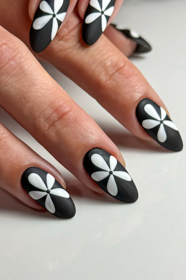 Black nail design with white flowers, floral art, matte finish, chic nail art inspiration.