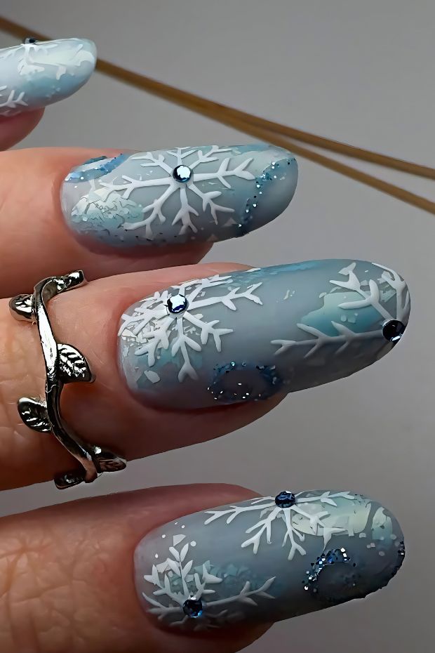 Winter nail design with snowflakes and rhinestones on a blue background for a festive touch.