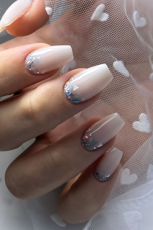 Chic winter nail design with nude gradient base and shimmering silver glitter tips for a festive look.