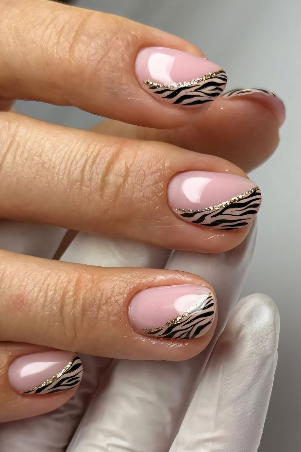 Stylish short nails with nude base, zebra print design, and gold accents for a trendy manicure.