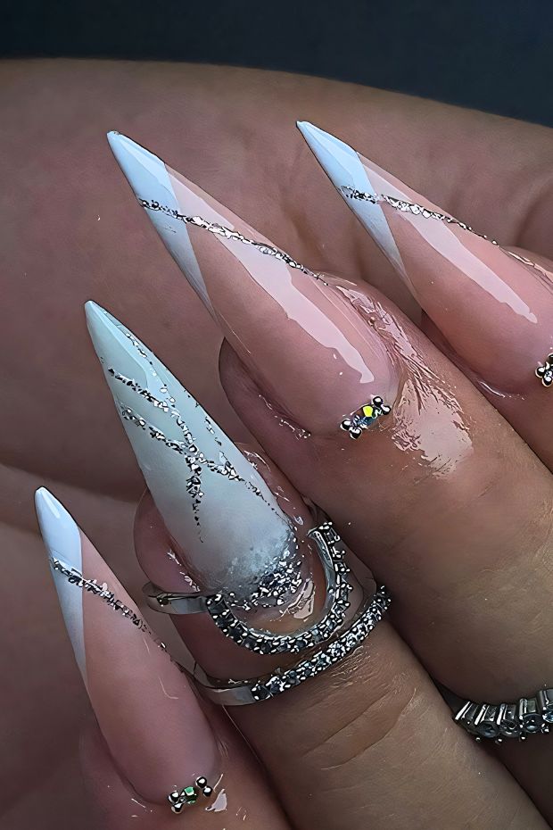 Stiletto nails featuring white and nude colors with silver geometric designs and accents for a modern nail art look.