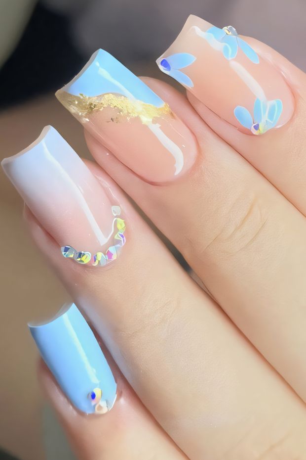 Creative birthday nails featuring blue accents, floral designs, gold shimmer, and elegant gems for a festive look.