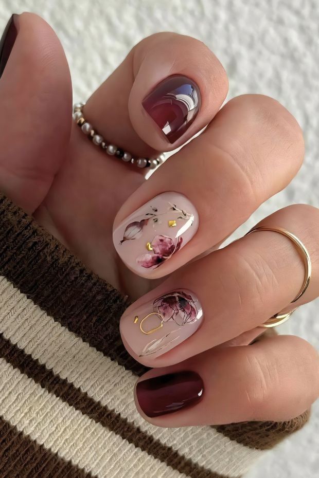 Chic short nails featuring burgundy and nude shades with floral designs and gold accents, perfect for elegant styles.