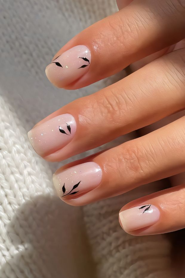 Minimalist nude nails with black leaf accents perfect for a stylish and subtle look.