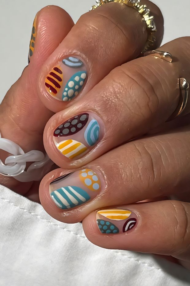 Colorful short nails featuring geometric patterns with stripes, dots, and vibrant hues.