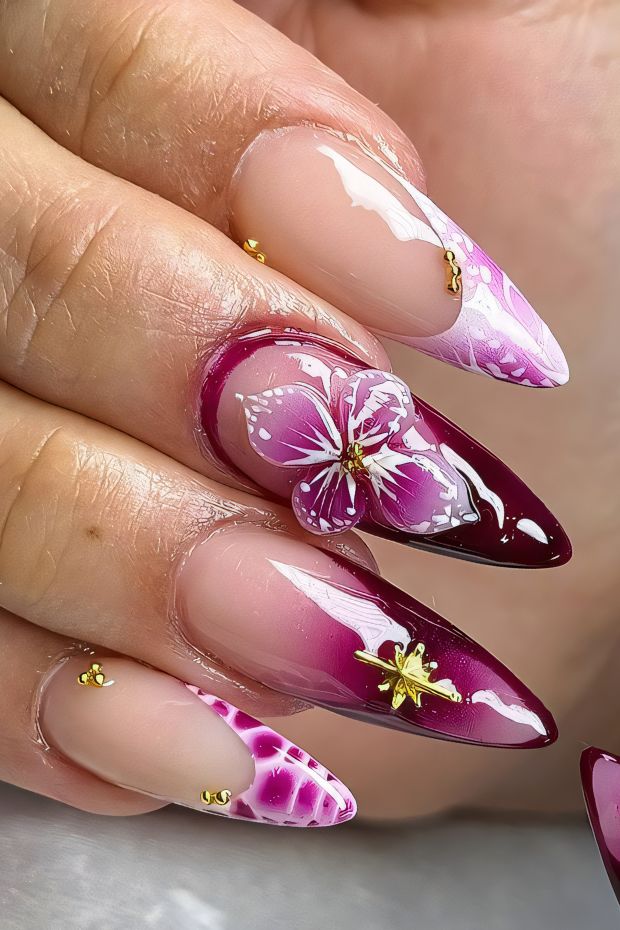 Stiletto nails with burgundy floral art and gold detailing for an elegant nail design.