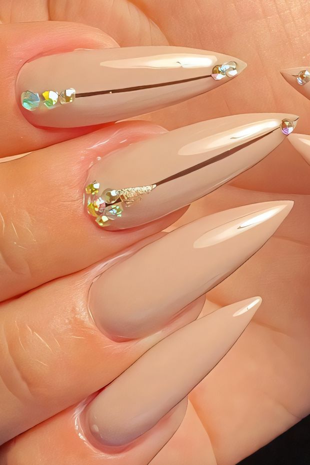 Nude stiletto nails decorated with crystals, showcasing a sleek and trendy nail design for modern nail art enthusiasts.