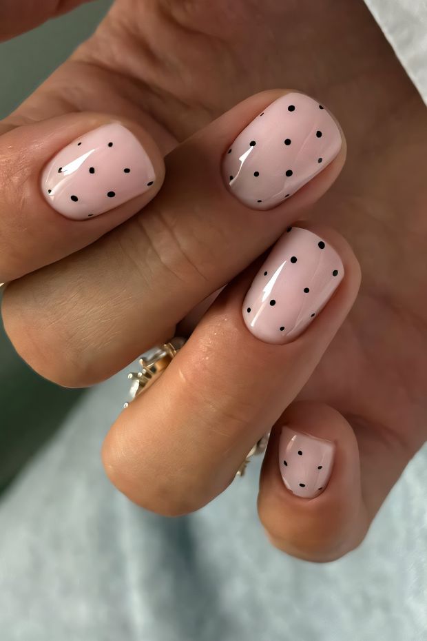 Short nails with blush pink base and black dots nail design for a chic minimalist style.