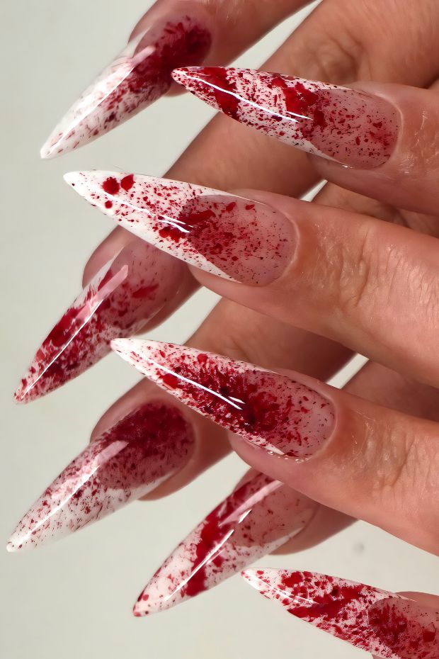 Glamorous stiletto nails featuring red blood splatter effects on a clear background for a dramatic look.