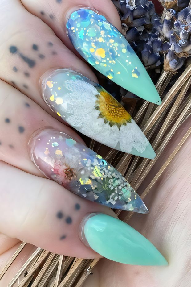 Vibrant stiletto nails featuring floral designs and glitter, showcasing a mix of colors and artistic elements.