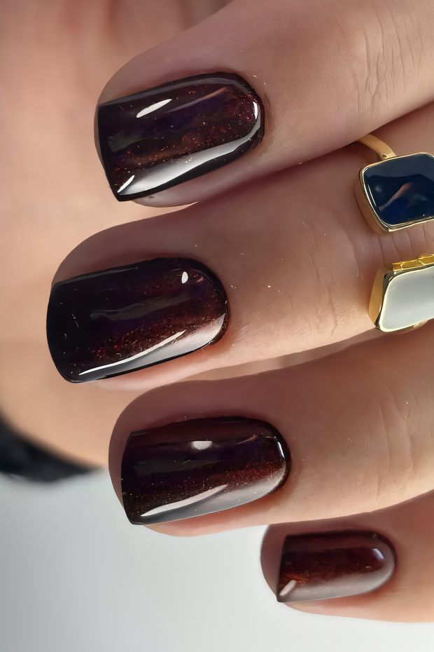 Short glossy dark red nails with shimmering accents featuring a sophisticated and elegant design for all occasions.