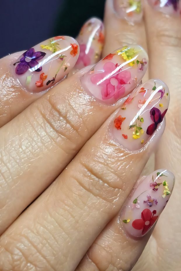 Colorful floral birthday nail art with translucent base, pink and purple flowers, and golden accents for a festive look.