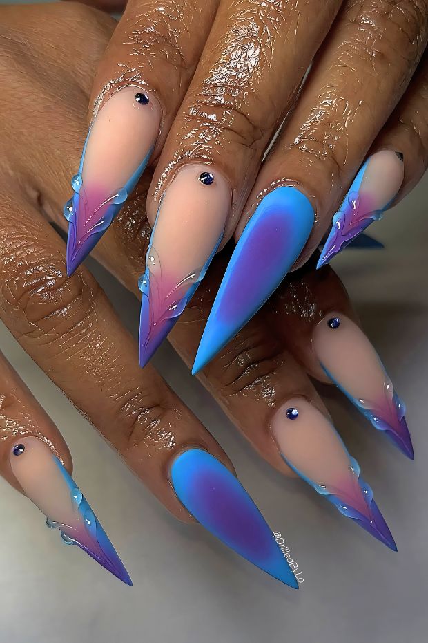 Stiletto nails with blue and purple ombre design, featuring decorative details and a glossy finish.