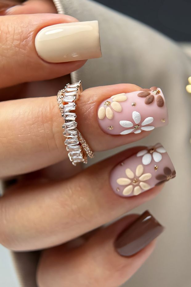 Brown nail design with floral patterns in soft colors and elegant rings, showcasing artistic nail art techniques.