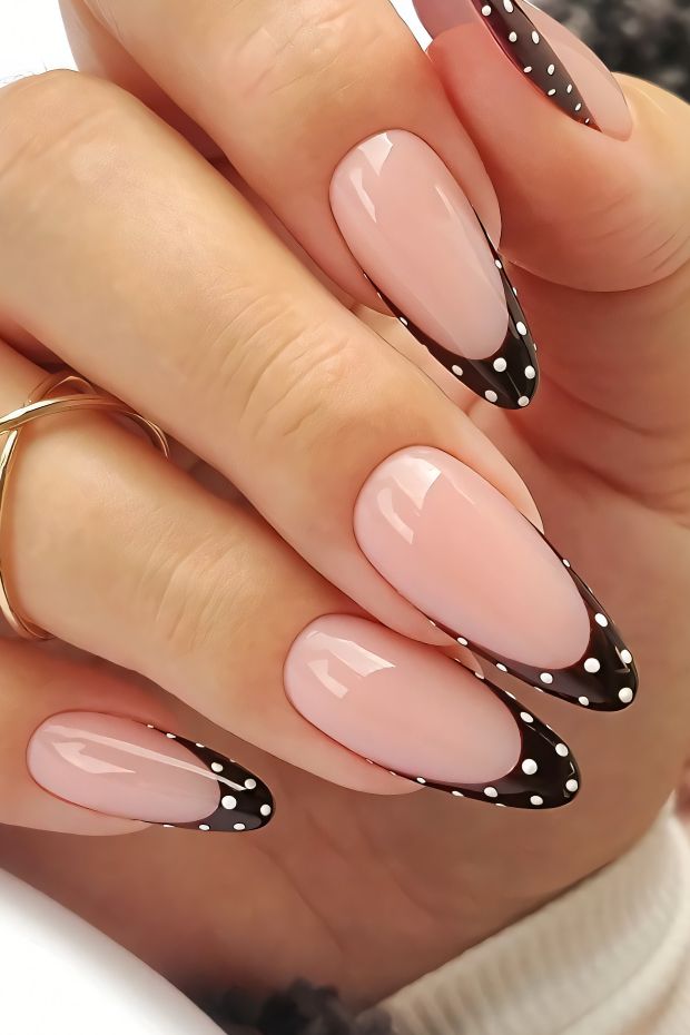 Nude nails with black tips and white polka dots for a stylish and modern nail art design.