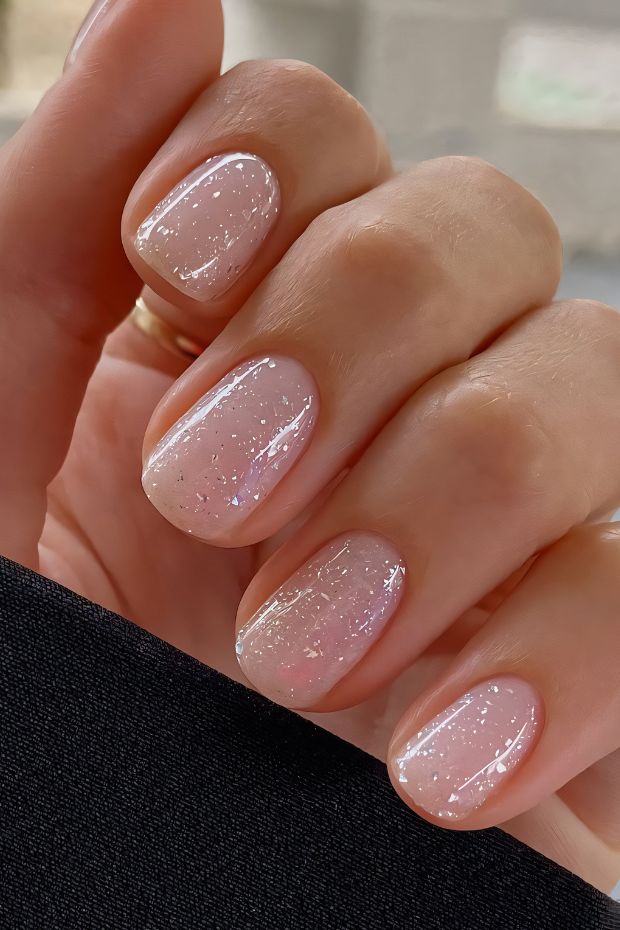 Elegant short nails with a soft pink base and sparkling glitter for a charming nail design.