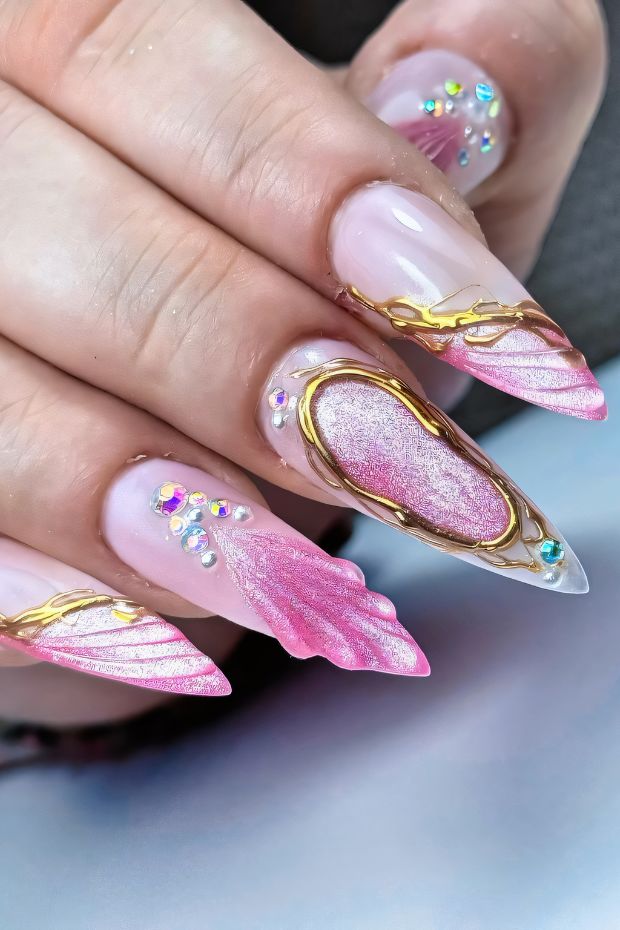 Stiletto nails with pink ombre, gold detailing, and crystal accents for a stylish nail art design.