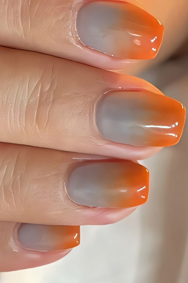 Gradient nail design featuring soft gray and vibrant orange hues for a trendy and stylish look.