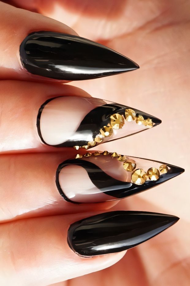 Glamorous stiletto nails featuring black polish, nude accents, and gold stud embellishments for a chic look.