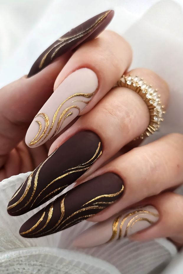 Elegant brown nails with gold swirl designs and nude accents for a sophisticated nail art style.