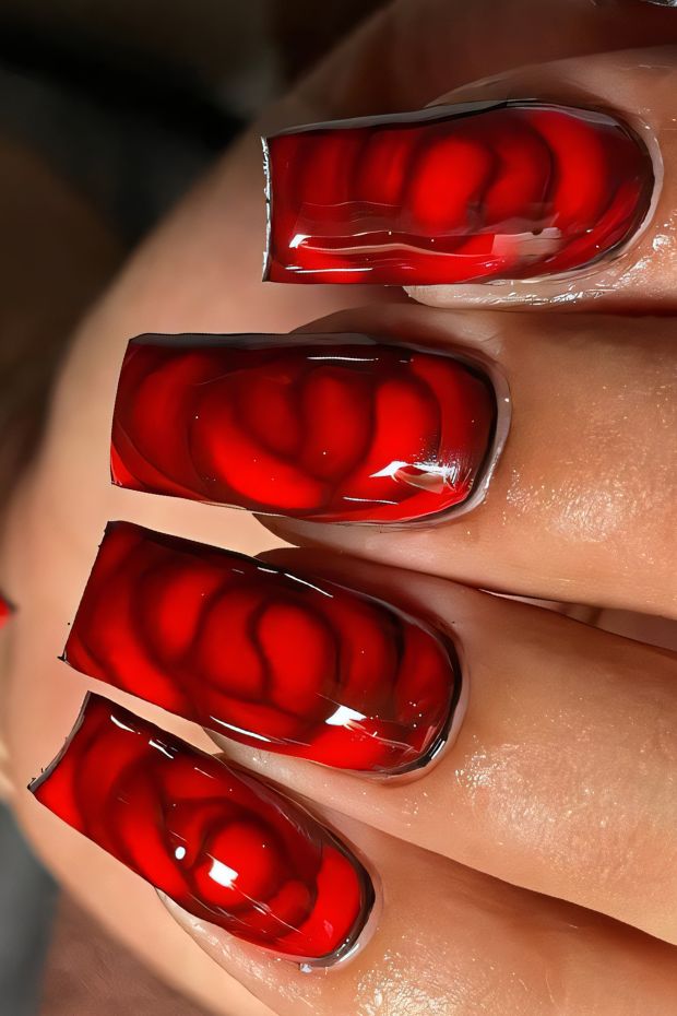 Vibrant red nails featuring a glossy finish and intricate 3D design, perfect for bold nail art.