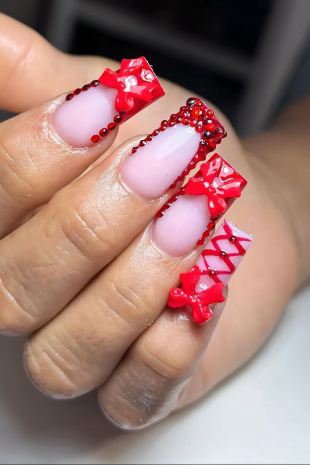 Stylish red nail design with bow accents and gems for a glamorous look.