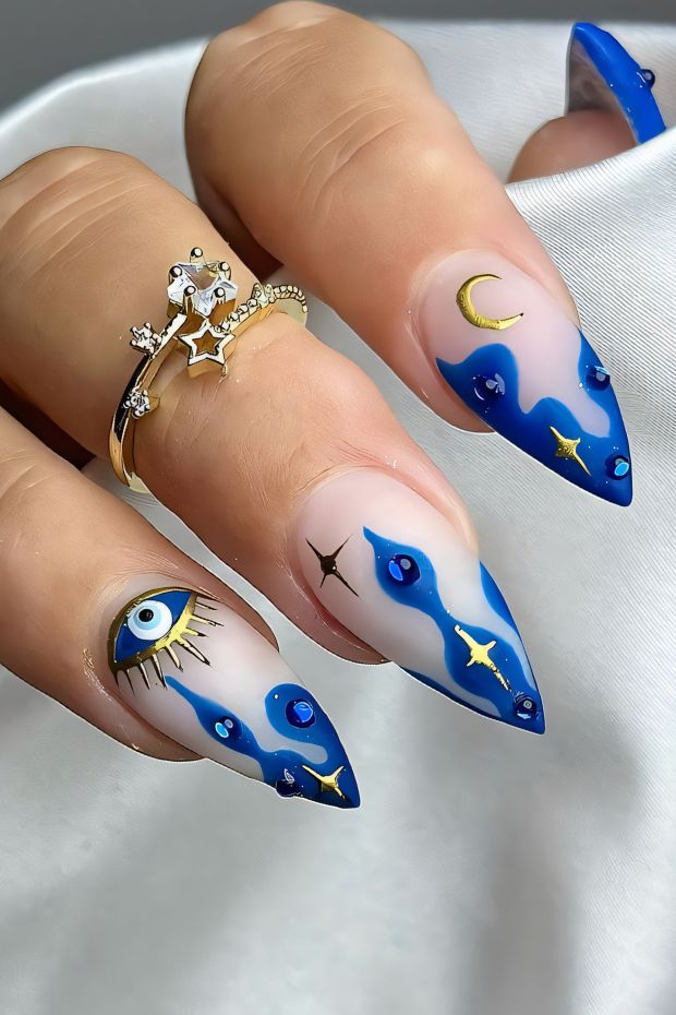 Blue and nude birthday nails with eye, crescent moon, stars, and embellishments for a celestial theme.