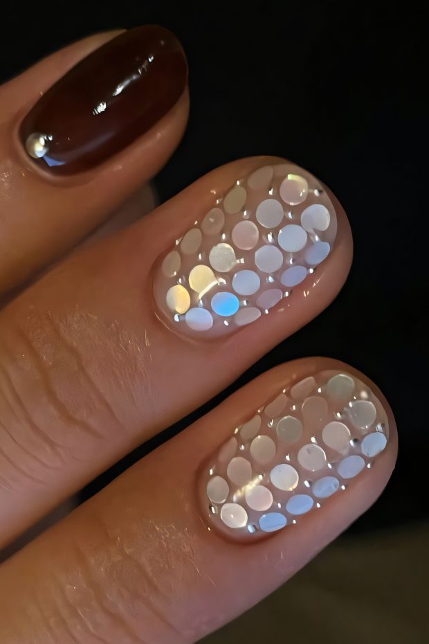 Chic nail design with a glossy brown accent and iridescent polka dot details on a neutral base.