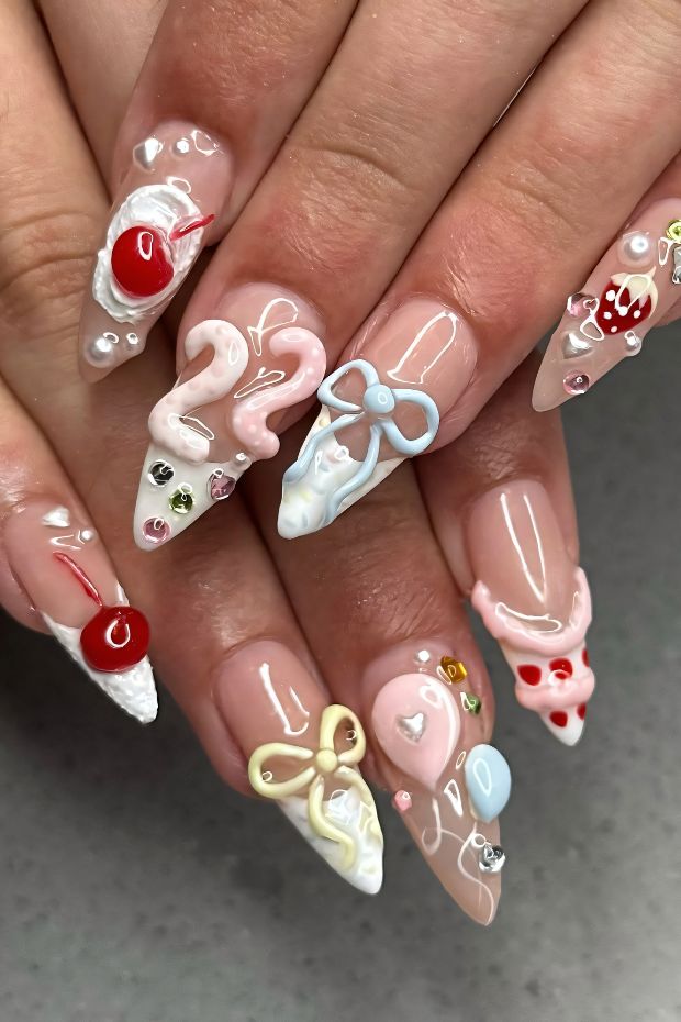 Colorful birthday-themed nail art with candy designs, bows, and embellishments on stylish long nails.