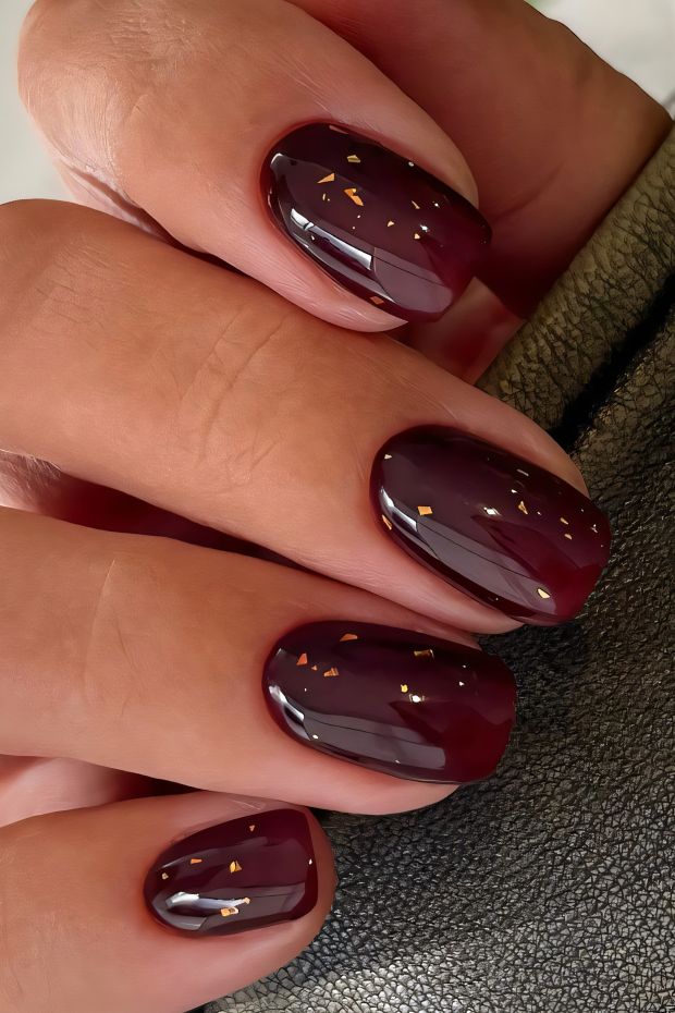 Chic burgundy nails featuring glossy finish with elegant gold flakes for a sophisticated nail design.