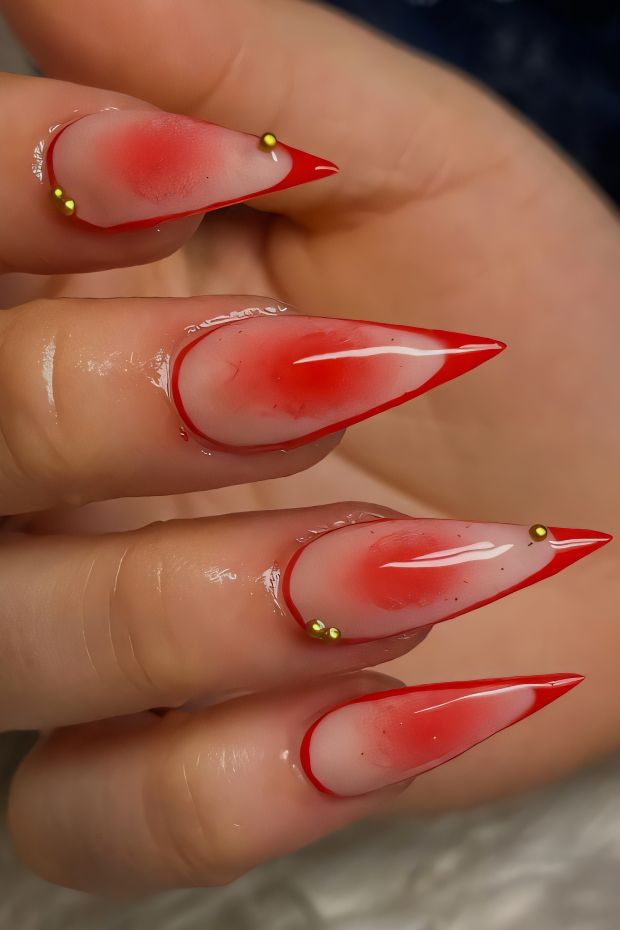 Ombre red almond nails with golden accent beads for a stylish and trendy manicure.