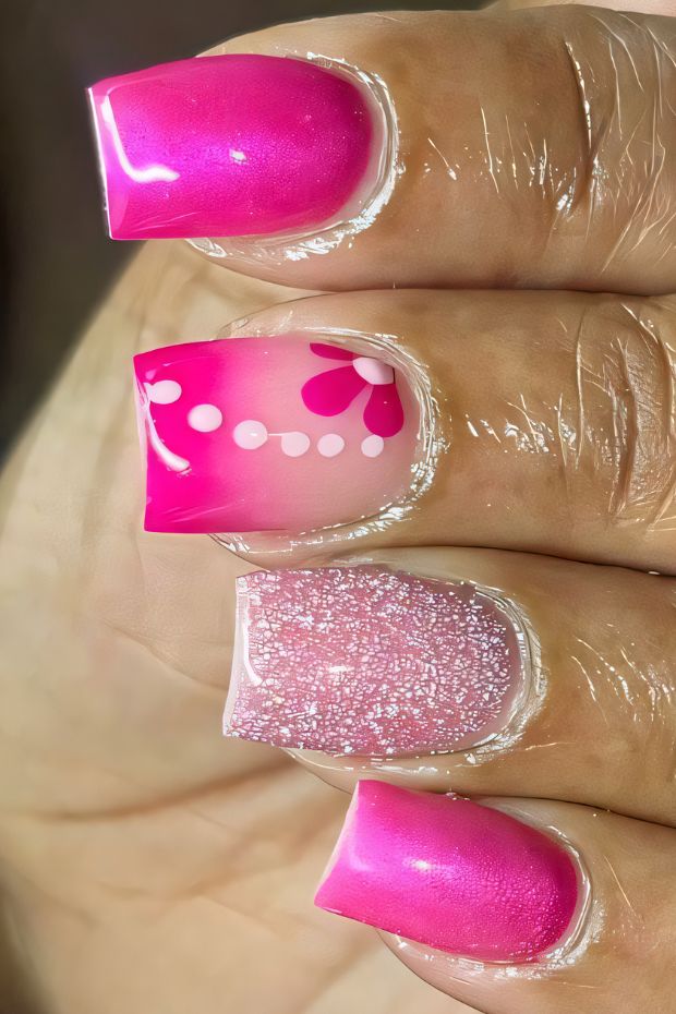 Short nails in vibrant pink with floral design and sparkly glitter accents for a stylish manicure.