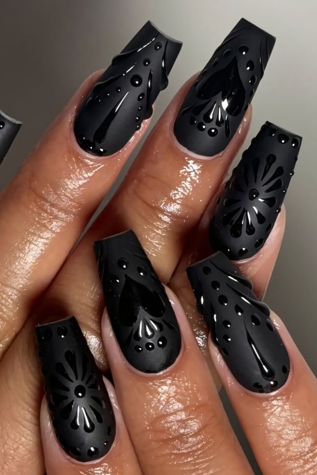 Matte black nails with 3D floral designs and glossy accents for a chic look.