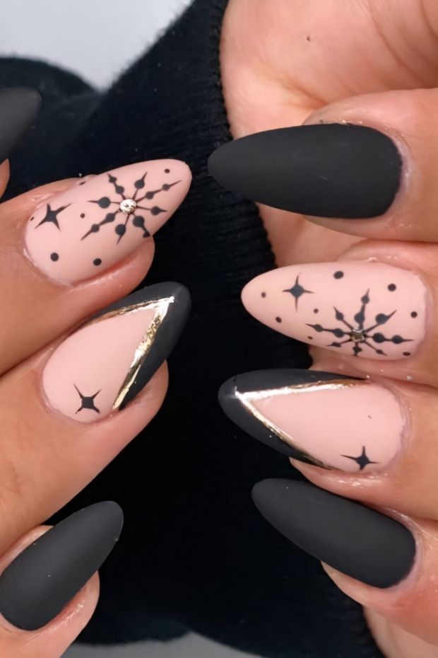 Stylish matte nail design featuring black and nude colors with intricate gold accents and star patterns.
